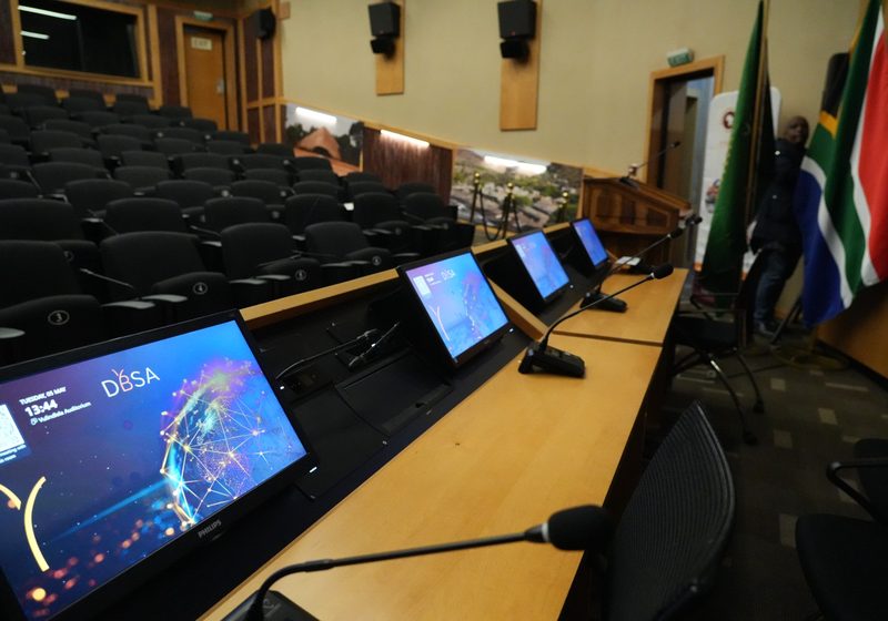 Boardroom collaboration room with screens, microphones and seating.