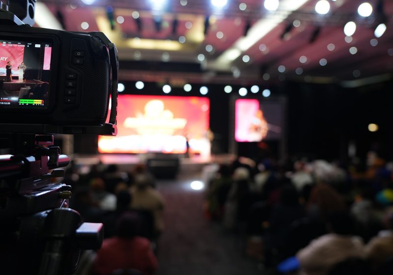 Professional camera in foreground capturing a live event stage and LED backdrop.