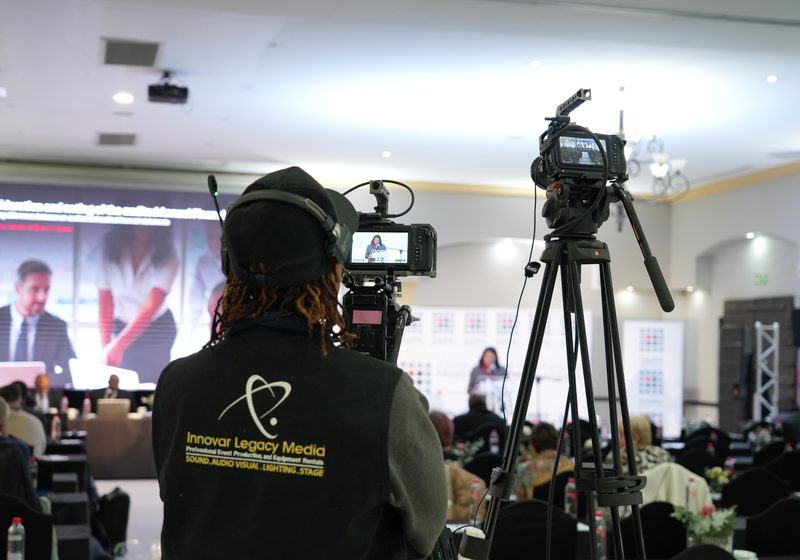 Camera operator filming a formal conference with two camera positions and audience.