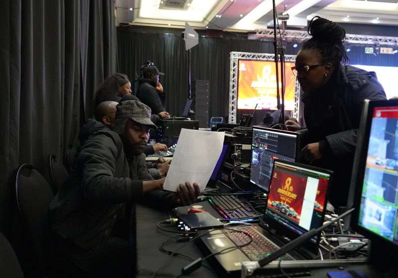 Technical crew coordinating from a live show-control desk with programme screens.