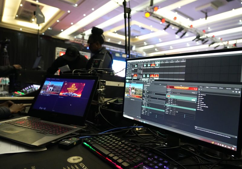 Technical desk with laptops and media playback software controlling event screen content.