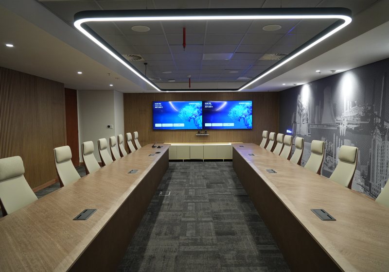 Two large wall displays above a credenza in a symmetrical executive boardroom with a long timber table