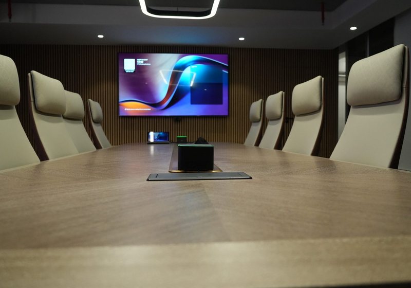 Executive boardroom with a long timber table, high-backed chairs and a wall display showing a presentation