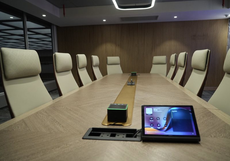 Touch control panel and microphone hub on a timber boardroom table with high-backed chairs