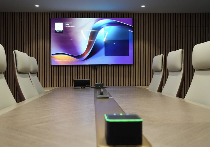 Table microphone hub in the foreground with a wall display beyond a long boardroom table