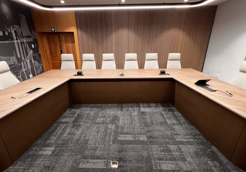 Wide view of a U-shaped boardroom table with microphones and connection points