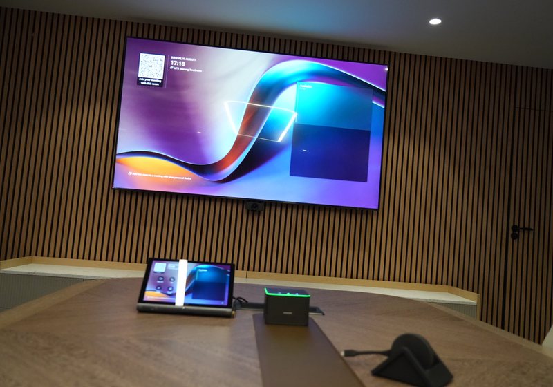Large wall display above a timber slat wall with a touch control panel on the table