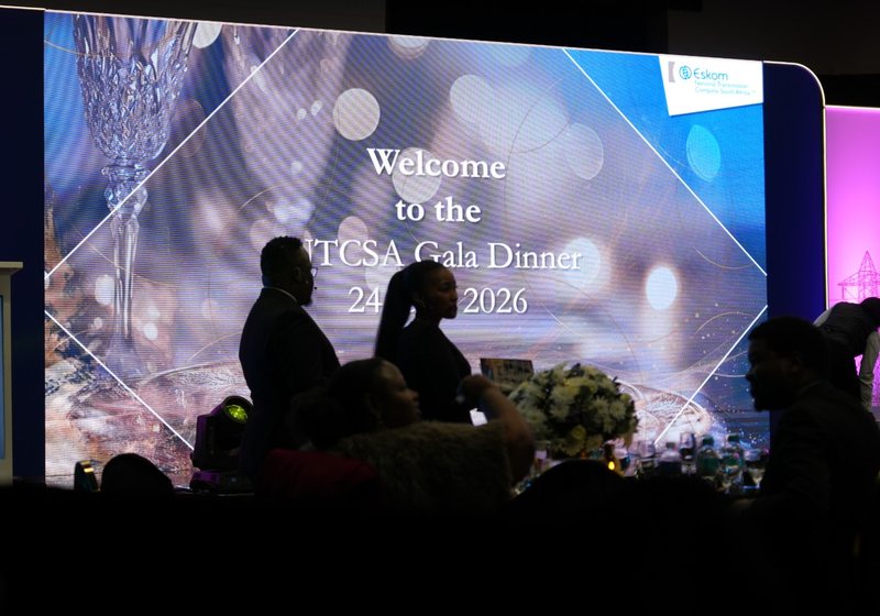Large LED wall showing a gala dinner welcome slide with silhouetted guests and branded purple-lit backdrops on either side