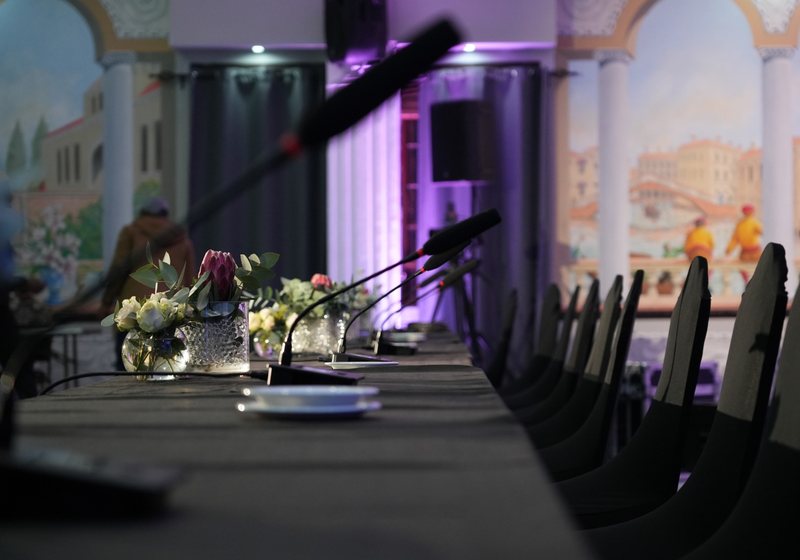 Row of gooseneck delegate microphones and small flower arrangements along a long black-draped table