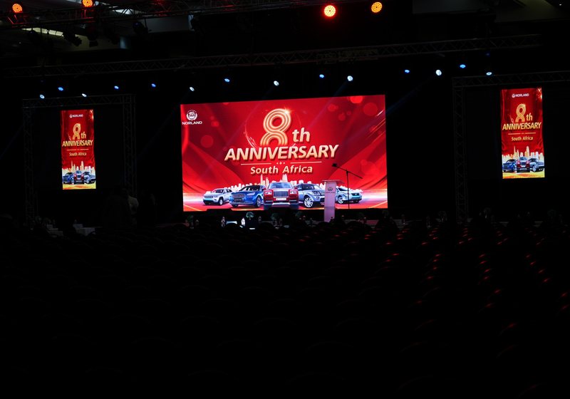 Wide LED main screen showing an 8th anniversary slide with two tall portrait LED screens on truss frames either side, in a dark hall