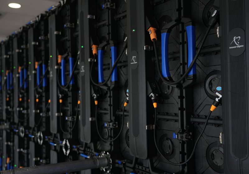 Rear of an LED wall showing black panel backs with blue handles, orange power connectors, data cables and Innovar Legacy branding