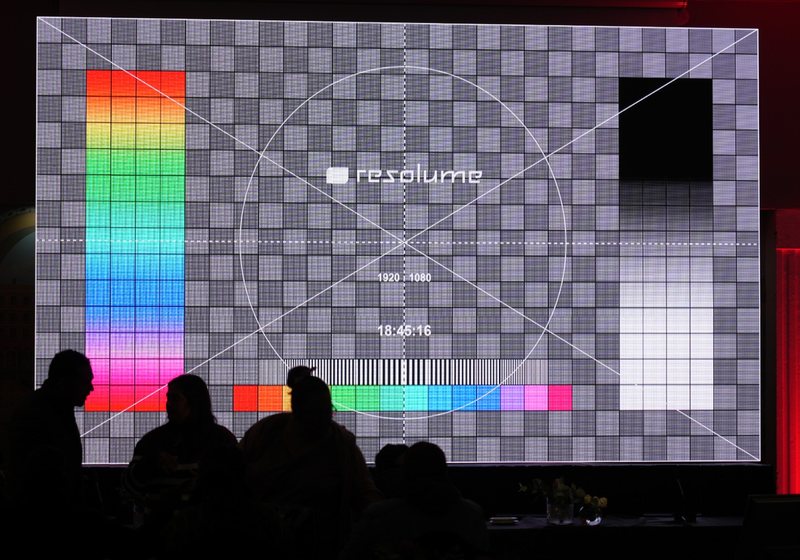 Large LED video wall showing a resolution test pattern with colour bars and grid, with silhouetted crew in front