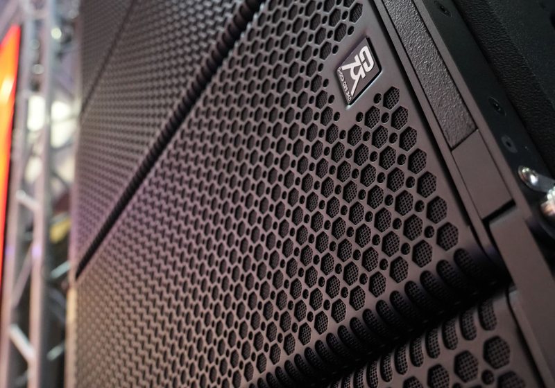Low angle close-up of stacked black line-array speaker cabinets with hexagonal grille pattern