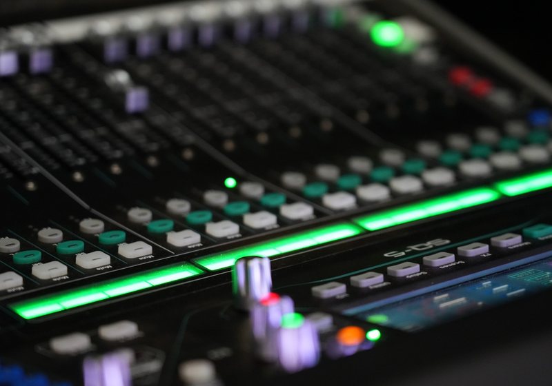 Close-up of a digital audio mixing console with green backlit strips, mute and select buttons and a touch screen