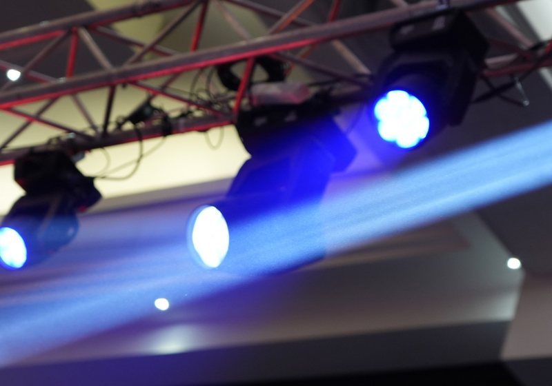 Four moving head lights on a truss throwing a blue beam of light through haze