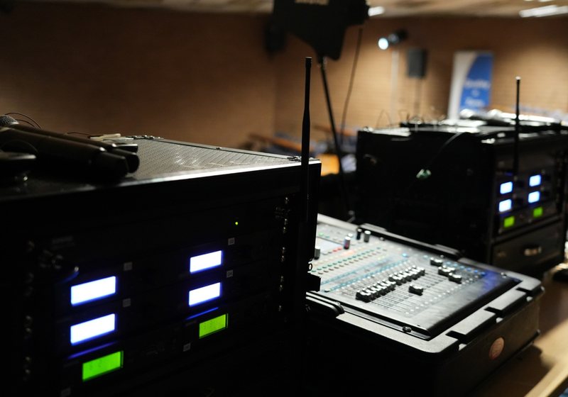 Rack-mounted wireless microphone receivers with glowing displays beside a compact digital mixing console in a dim room