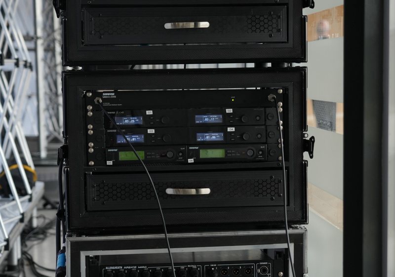 Stacked flight-case racks holding wireless microphone receivers, an audio stage box and a power amplifier with cables connected
