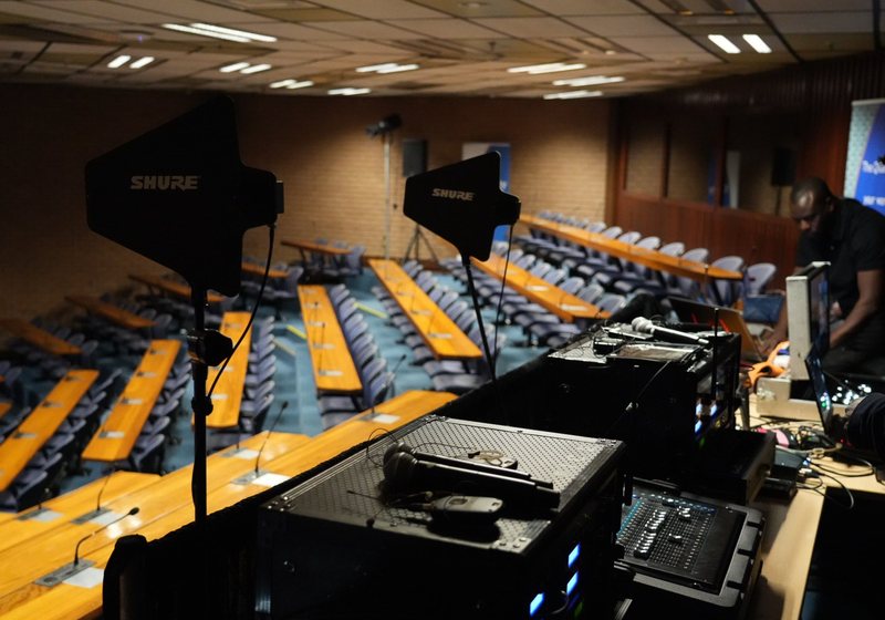 Two wireless antennas and equipment racks at the back of a tiered auditorium with wooden desks and desk microphones